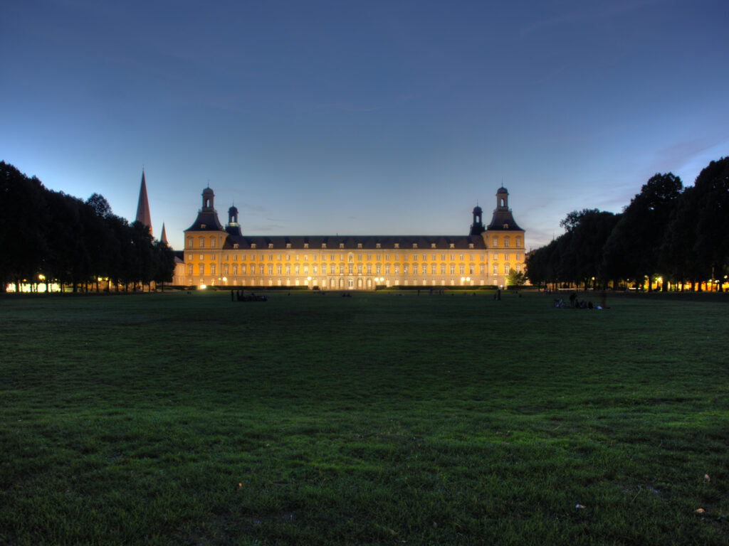 Das gelbe Universäsitasgebäude am Abend angestrahlt vor dunkelblauem Himmel